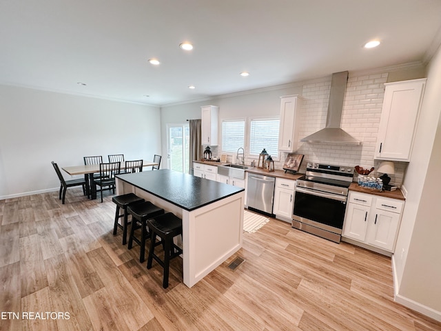 kitchen featuring wall chimney exhaust hood, stainless steel appliances, a center island, and white cabinets