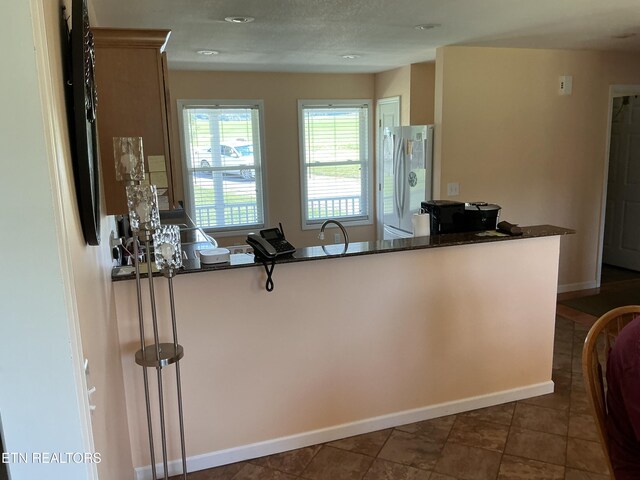 kitchen with dark stone counters, dark tile patterned floors, sink, kitchen peninsula, and stainless steel refrigerator