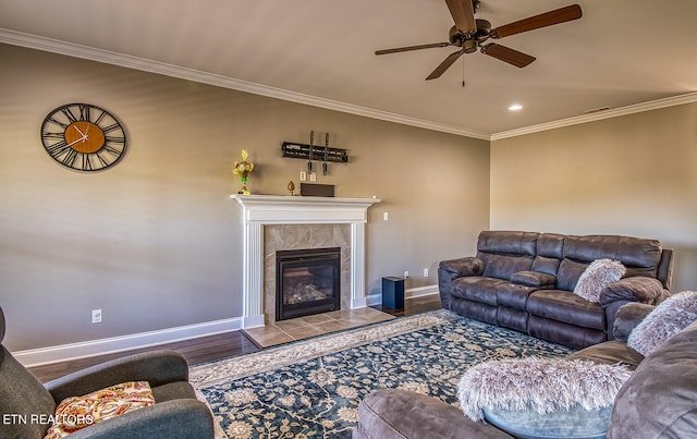 living room featuring ceiling fan, wood-type flooring, a tiled fireplace, and ornamental molding