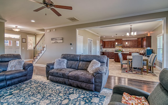 living room with light wood-type flooring, ceiling fan with notable chandelier, and crown molding