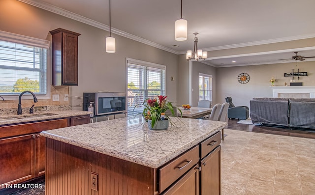 kitchen featuring a tiled fireplace, sink, crown molding, a center island, and pendant lighting