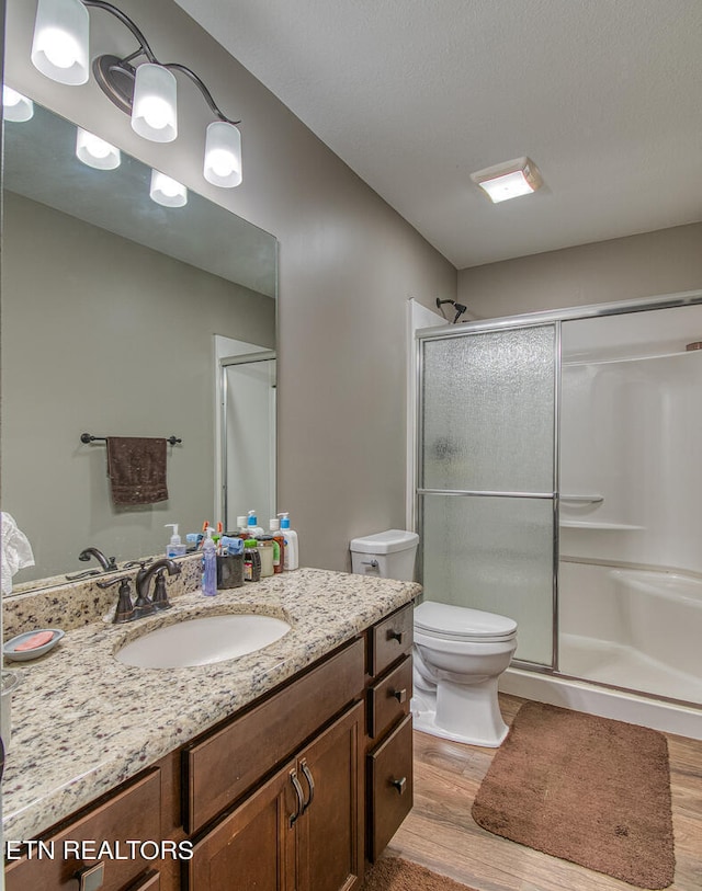 bathroom with toilet, vanity, wood-type flooring, and a shower with shower door