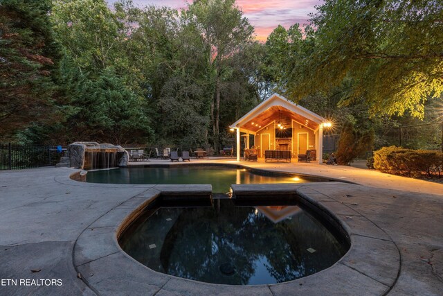 pool at dusk with a patio and an in ground hot tub