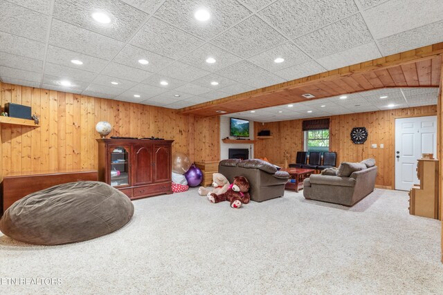 living room featuring a drop ceiling, wooden walls, and carpet floors