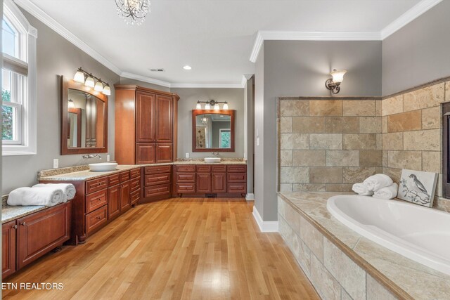 bathroom with hardwood / wood-style floors, tiled tub, vanity, and crown molding