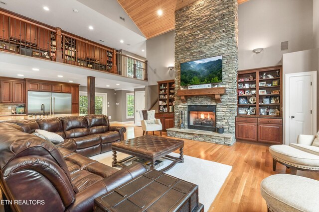 living room featuring high vaulted ceiling, light hardwood / wood-style floors, and a stone fireplace