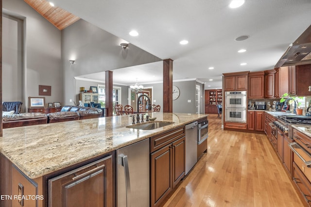 kitchen with sink, a large island with sink, appliances with stainless steel finishes, an inviting chandelier, and light hardwood / wood-style floors