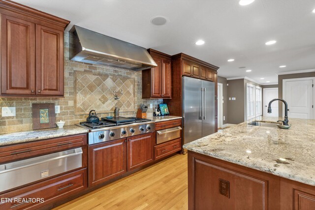 kitchen with sink, light hardwood / wood-style flooring, wall chimney range hood, appliances with stainless steel finishes, and crown molding