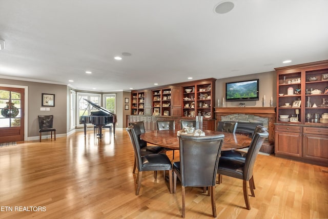 dining area with a stone fireplace, light wood-type flooring, and ornamental molding