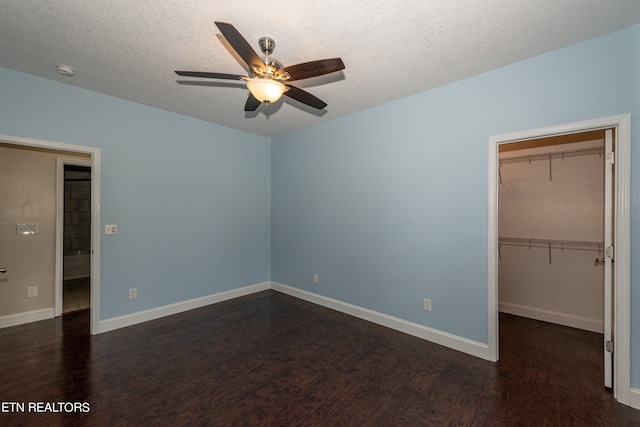 unfurnished bedroom with ceiling fan, a textured ceiling, dark wood-type flooring, and a spacious closet