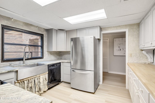 kitchen featuring stainless steel refrigerator, black dishwasher, light wood-type flooring, a drop ceiling, and sink