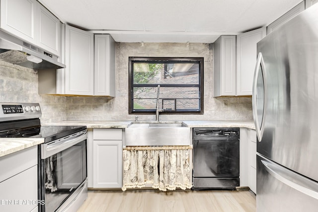 kitchen with light stone counters, stainless steel appliances, light wood-type flooring, sink, and extractor fan