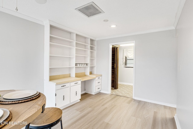 interior space featuring light wood-type flooring, crown molding, a textured ceiling, and built in desk