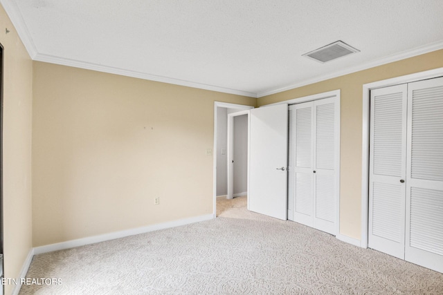 unfurnished bedroom featuring a textured ceiling, ornamental molding, light carpet, and multiple closets