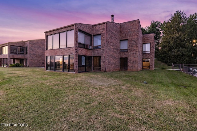 back house at dusk featuring a lawn