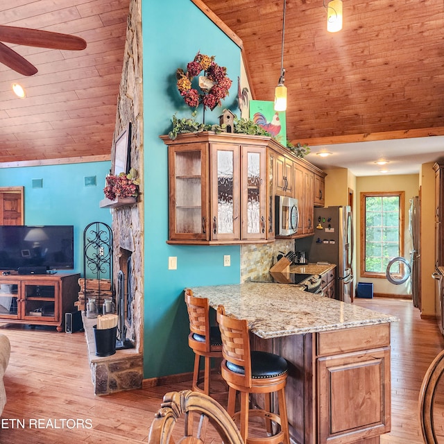 kitchen featuring ceiling fan, light hardwood / wood-style floors, kitchen peninsula, stainless steel appliances, and a kitchen bar