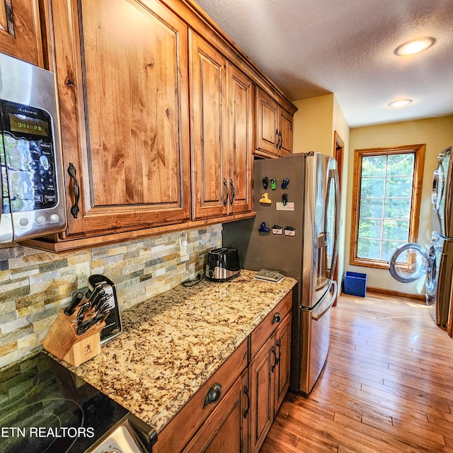 kitchen with a textured ceiling, light hardwood / wood-style flooring, decorative backsplash, appliances with stainless steel finishes, and light stone countertops