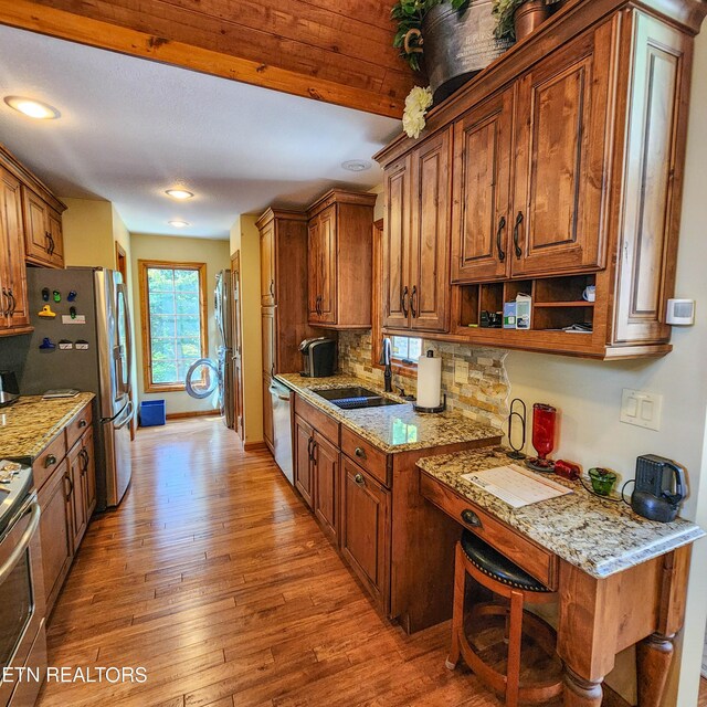 kitchen with tasteful backsplash, sink, light hardwood / wood-style flooring, stainless steel appliances, and light stone countertops