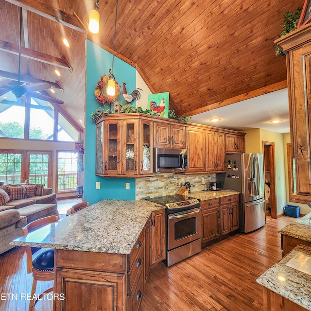 kitchen with wood-type flooring, decorative light fixtures, high vaulted ceiling, stainless steel appliances, and a breakfast bar