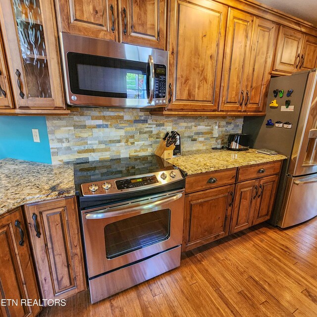 kitchen with light stone countertops, stainless steel appliances, backsplash, and light wood-type flooring