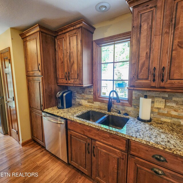 kitchen featuring light wood-type flooring, sink, stainless steel dishwasher, backsplash, and light stone countertops