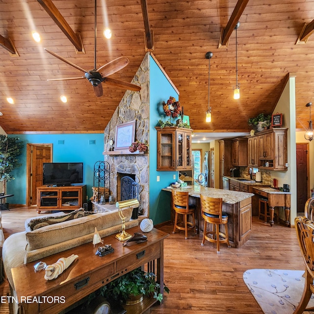 living room with light hardwood / wood-style floors, high vaulted ceiling, a stone fireplace, ceiling fan, and wooden ceiling