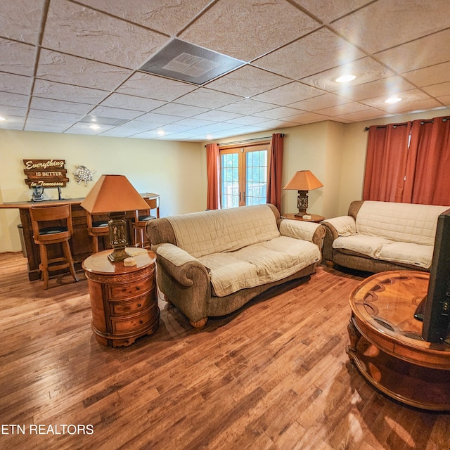 living room with bar area, a drop ceiling, and hardwood / wood-style floors