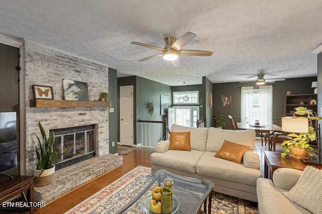 living room with ceiling fan, a textured ceiling, a fireplace, and hardwood / wood-style flooring