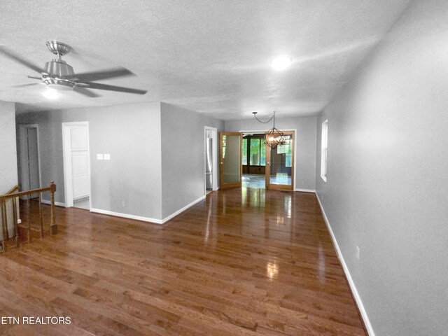 spare room featuring a textured ceiling, ceiling fan with notable chandelier, and dark wood-type flooring