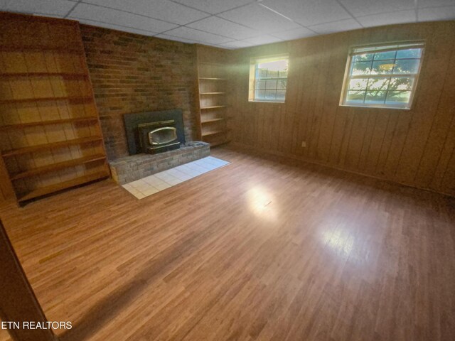 unfurnished living room with a paneled ceiling, wood-type flooring, and a brick fireplace