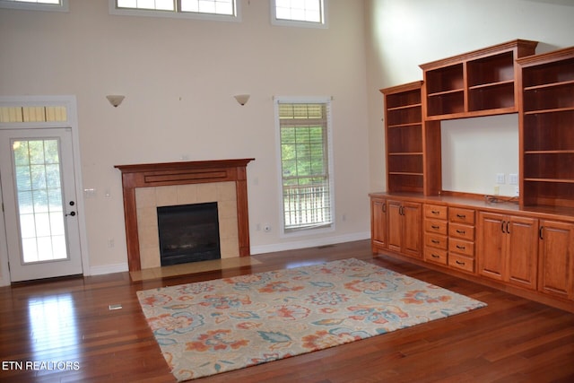 unfurnished living room featuring a tile fireplace, dark hardwood / wood-style floors, and a healthy amount of sunlight