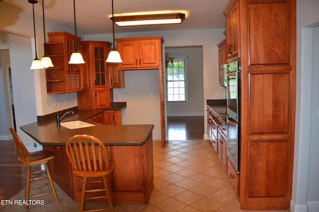 kitchen with pendant lighting, light tile patterned floors, sink, kitchen peninsula, and a kitchen breakfast bar