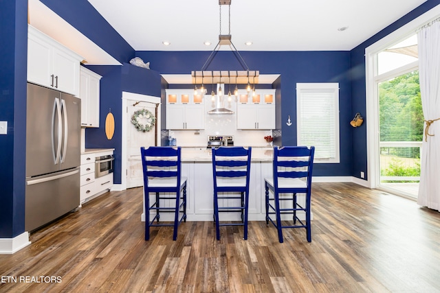 kitchen with white cabinets, decorative light fixtures, an island with sink, and stainless steel appliances