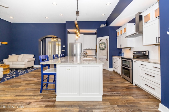 kitchen with appliances with stainless steel finishes, dark hardwood / wood-style floors, an island with sink, hanging light fixtures, and white cabinets