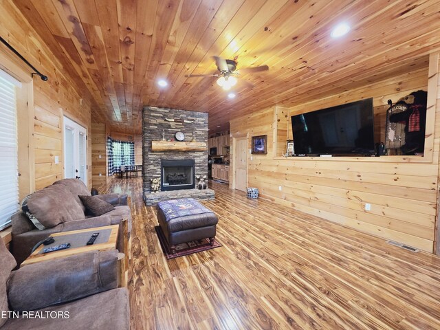 living room with ceiling fan, a fireplace, wood walls, and wood-type flooring