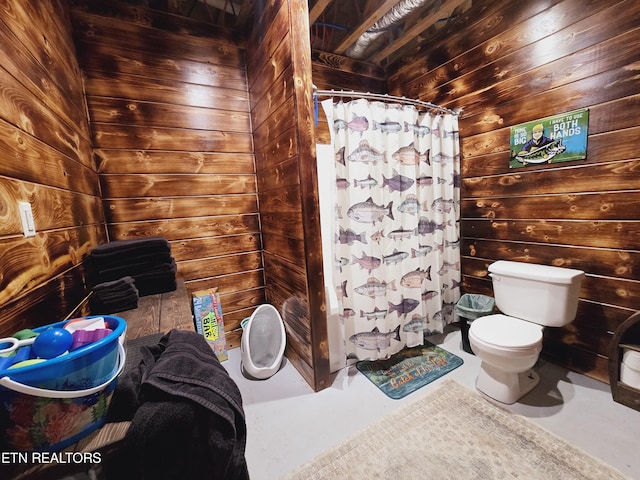 bathroom featuring a shower with shower curtain, wooden walls, toilet, and concrete flooring
