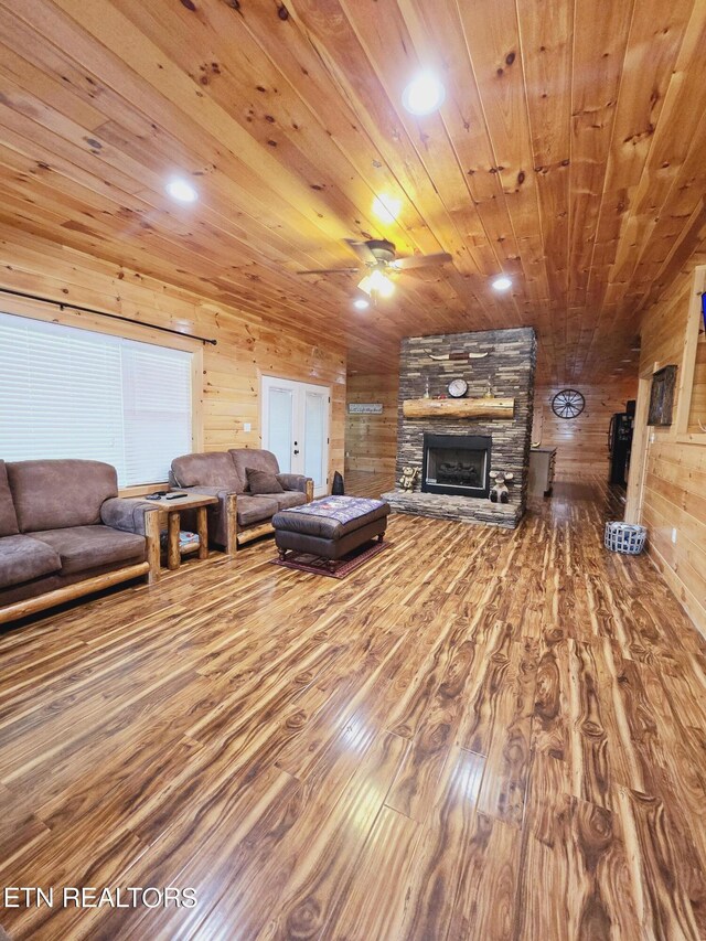 living room featuring wooden walls, ceiling fan, wooden ceiling, and a stone fireplace