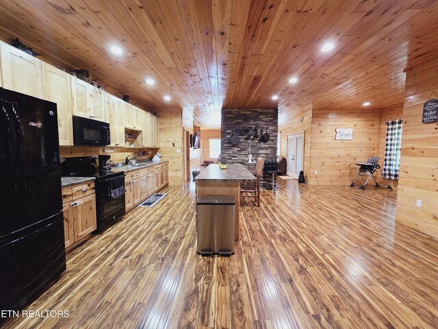 kitchen with light brown cabinets, black appliances, wood-type flooring, wooden walls, and sink