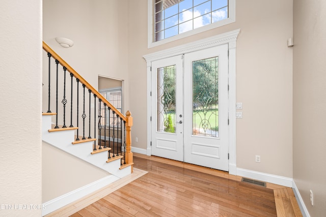 foyer entrance featuring a healthy amount of sunlight, a towering ceiling, light hardwood / wood-style flooring, and french doors