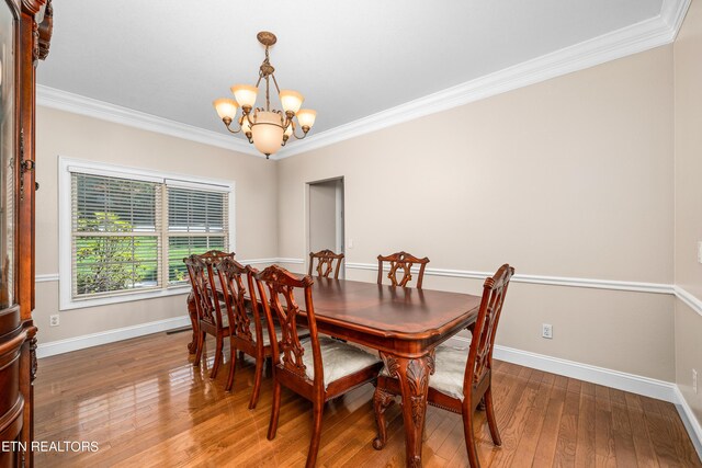 dining room featuring wood-type flooring, ornamental molding, and an inviting chandelier