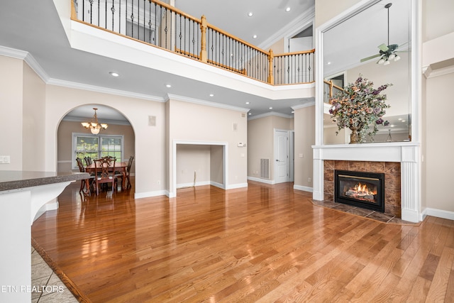 unfurnished living room with a high ceiling, ceiling fan with notable chandelier, a fireplace, and light wood-type flooring