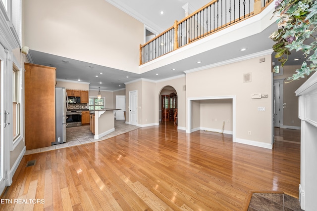 unfurnished living room featuring ornamental molding, a high ceiling, and light hardwood / wood-style floors