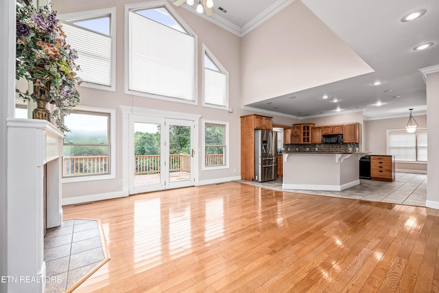 unfurnished living room with light wood-type flooring, a towering ceiling, and ornamental molding