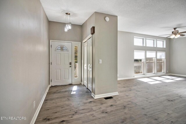 entrance foyer with ceiling fan with notable chandelier, a towering ceiling, a textured ceiling, and hardwood / wood-style flooring