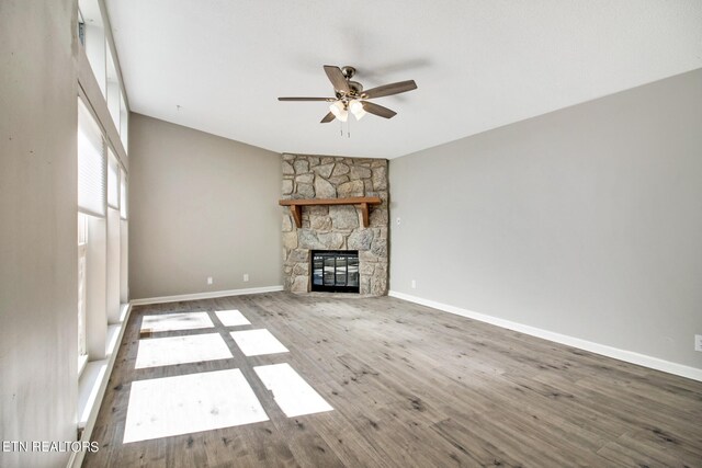 unfurnished living room featuring a stone fireplace, hardwood / wood-style floors, and ceiling fan