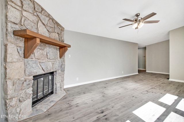 unfurnished living room featuring ceiling fan, a stone fireplace, and wood-type flooring