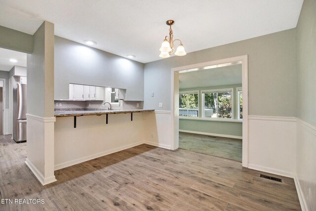 kitchen featuring stainless steel fridge, white cabinets, kitchen peninsula, a kitchen bar, and light hardwood / wood-style flooring