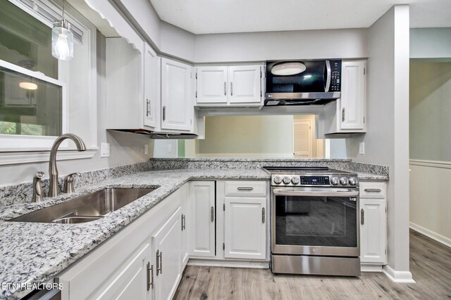 kitchen with appliances with stainless steel finishes, hanging light fixtures, white cabinets, light wood-type flooring, and sink