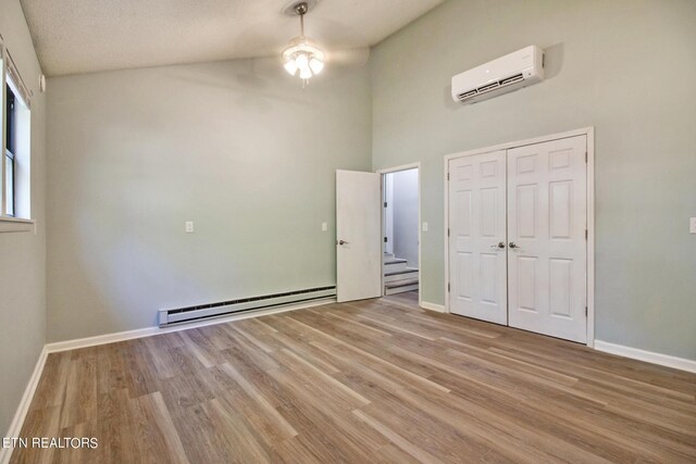 unfurnished bedroom featuring a textured ceiling, light hardwood / wood-style flooring, a baseboard heating unit, a closet, and an AC wall unit