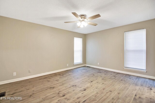 spare room featuring light wood-type flooring, a textured ceiling, ceiling fan, and plenty of natural light